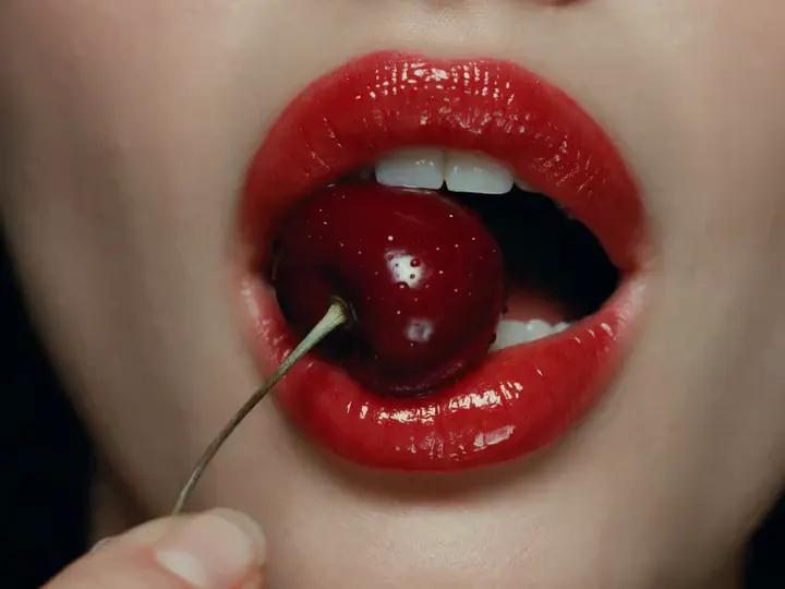 Glossy red lips press softly around a wet dark cherry.